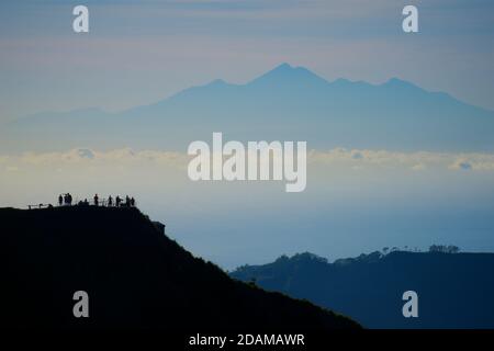 Monte Rinjani a Lombok visto da una salita del Monte Batur, Bali, Indonesia. Silhouette di escursionisti contro la fresca luce del mattino. Foto Stock