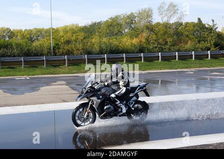 Pilota che fa aquaplaning o prove di aquaplaning su una motocicletta che accelera lungo una strada bagnata per vedere quando gli pneumatici inizia a perdere il contatto con il surf Foto Stock