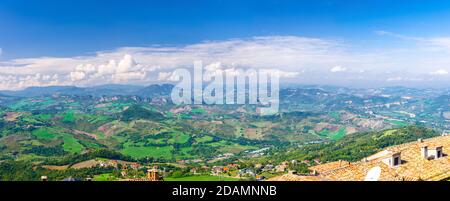 Vista panoramica dall'alto del paesaggio con valle, verdi colline, campi e villaggi della Repubblica San Marino quartiere suburbano con cielo blu bianco nuvole sfondo. Vista dalla fortezza di San Marino. Foto Stock