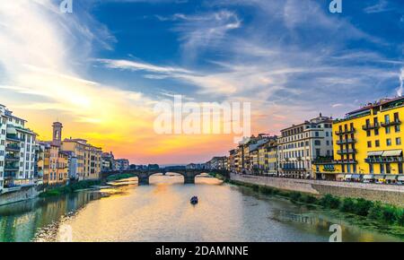 Ponte in pietra e barca sul fiume Arno e passeggiata a terrapieno con edifici nel centro storico di Firenze, blu brillante Foto Stock