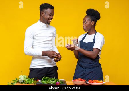 coppie africane che cucinano insieme, che discutono che cosa fare, donna che tiene una cipolla Foto Stock