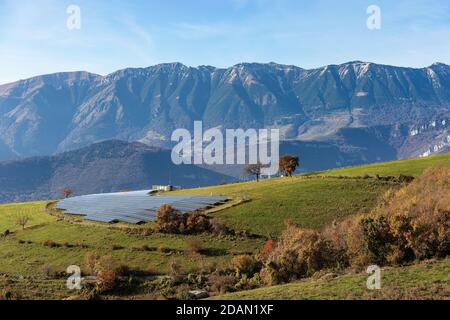 Centrale solare nelle Alpi italiane con numerosi pannelli solari, Altopiano Lessinia con la catena montuosa del Monte Baldo. Italia. Concetto di energia rinnovabile. Foto Stock