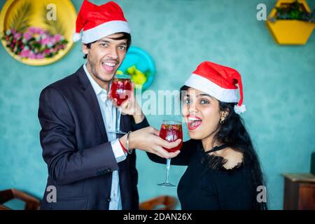 Felice giovane coppia in cappelli di santa che festeggiano il Natale insieme mentre si diverte con gli occhiali rossi cocktail drink amore, bonding, copia spazio. Foto Stock