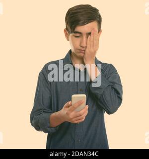 Studio girato di giovane ragazzo persiano stressato adolescente utilizzando il cellulare telefono mentre copra il viso Foto Stock