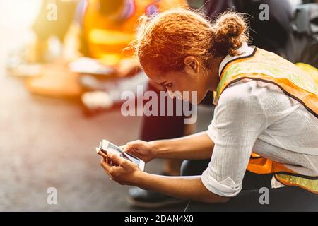 Black African American break si rilassa e legge le notizie sul suo smartphone mobile in una fabbrica industriale. Foto Stock