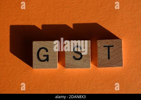 Acronimo di GST per Gods and Services Tax, in lettere alfabetiche in legno isolate su sfondo arancione