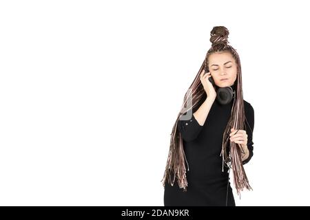 Ritratto di bella ragazza con lunghe frotrecce rosa che ascolta la musica in grandi cuffie e con grazia piegarsi. Studio shot su sfondo bianco Foto Stock