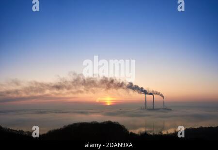 Splendida vista del cielo blu e rosa colorato con il sole luminoso che sorge presso la centrale termoelettrica. Camini termici che producono fumo denso con gas tossici in atmosfera. Concetto di generazione di energia. Foto Stock