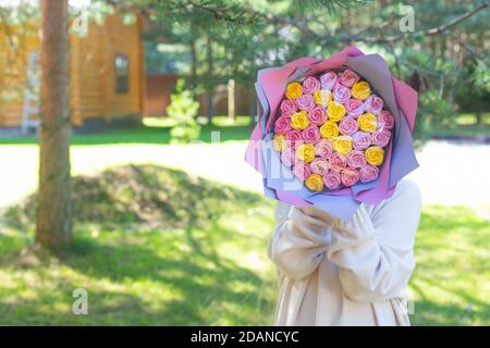 Una ragazza in un maglione leggero in natura e coperto il suo volto con un bouquet di rose multicolore. Festa della mamma, compleanno, congratulazioni, regalo Foto Stock
