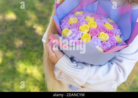 Un bouquet di lilla e rose gialle è decorato in carta multicolore nelle mani di una ragazza su uno sfondo verde naturale. Un mazzo di fiori Foto Stock