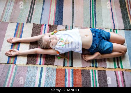 Ragazza caucasica con trecce in una T-shirt bianca sta facendo yoga, che si allunga a casa su un tappeto di tessuto a righe.Detox digitale, riunione con la natura, sano br Foto Stock