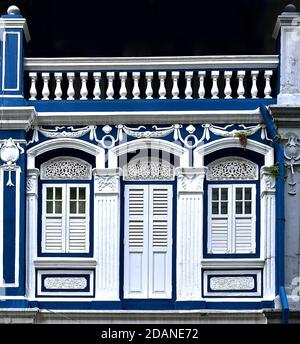 Restaurata bottega cinese peranakan con persiane in legno bianco e archi ornati e architrave su uno sfondo blu scuro. Foto Stock