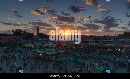 Piazza Yamaa el Fna con i suoi mercati e la folla di persone e la torre della moschea sullo sfondo, al tramonto. Concetto di viaggio. Marrakech, Marocco Foto Stock