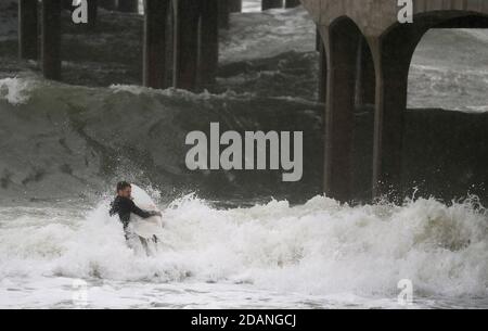 Un surfista affronta grandi onde mentre fanno la loro strada verso il mare al largo della spiaggia di Boscombe in Dorset. Foto Stock