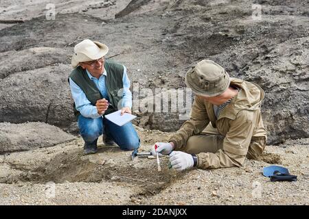 due paleontologi maschili nel deserto discutono il ritrovamento e. prendere appunti in un notebook da campo Foto Stock