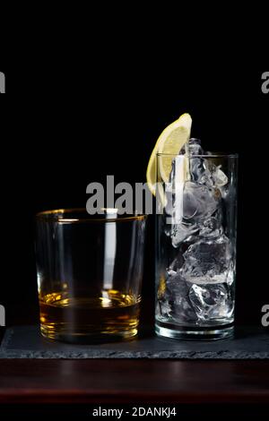 Whisky pulito e un bicchiere di ghiaccio servito su un piatto di ardesia. Tavolo in legno rosso scuro, alta risoluzione Foto Stock