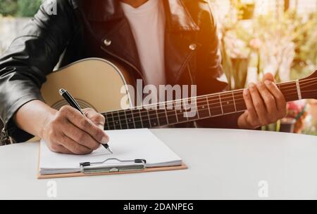 Un autore di canzoni che tiene una penna per comporre un brano. Musicista che suona la chitarra acustica. Musica dal vivo e concetto musicale astratto. Foto Stock