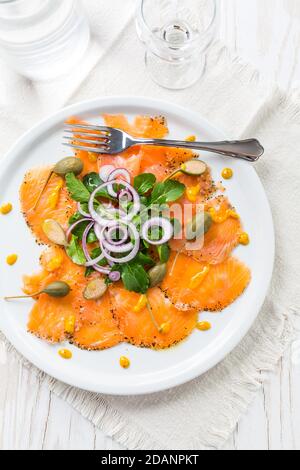Carpaccio di salmone e insalata di rucola con cipolle e capperi piastra bianca Foto Stock