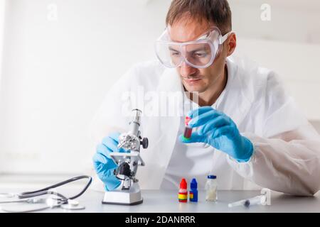 Un maschio di medico o scienziato guardando attraverso un microscopio su un tavolo con il computer portatile in background Foto Stock