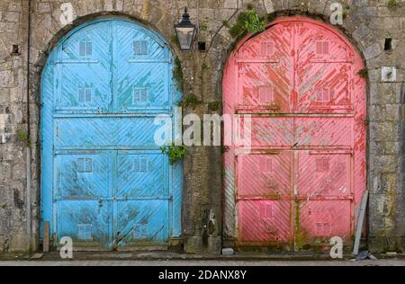 Coppia di grandi e colorate vecchie porte con sbucciatura allestita in un edificio in pietra. Foto Stock