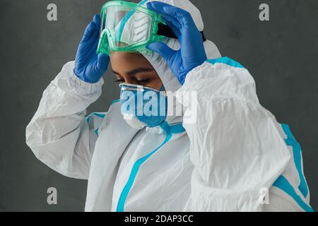 Specialista medico femminile che indossa occhiali protettivi. Medico in tuta protettiva che si prepara al lavoro durante una pandemia. Foto Stock