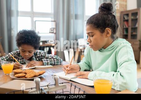 Diligente studentessa e il suo fratello carino che fa note in copybooks per tabella Foto Stock