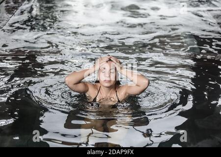 Angolo di tranquilla giovane femmina ottenere vasca idromassaggio in piscina con acqua pulita mentre riposa durante il fine settimana nel centro benessere centro Foto Stock