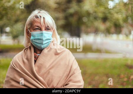 Donna che indossa maschera protettiva e in una sciarpa calda di cashmere in parco all'aperto durante la quarantena di pandemia di coronavirus. Copia, spazio vuoto per il testo Foto Stock