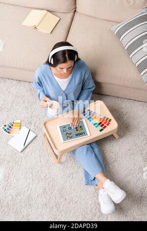 Giovane donna designer in pigiama blu e cuffie su cui lavorare il pavimento Foto Stock
