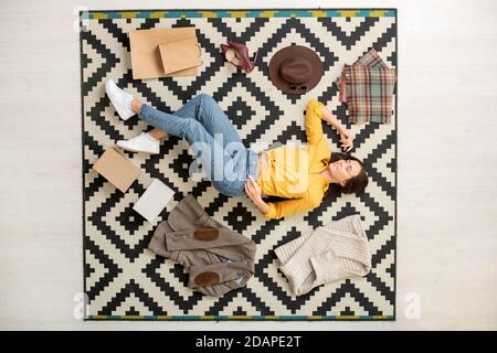 Vista della giovane donna felice circondata da nuovo casualwear intelligente sdraiato sul tappeto Foto Stock