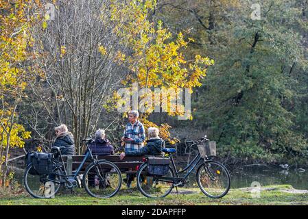 I ciclisti anziani riposano sulla panchina del parco lungo il lago in autunno foresta Foto Stock