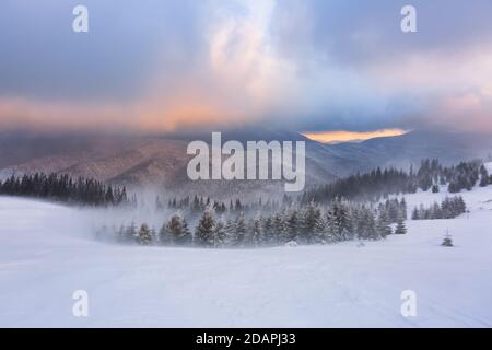 L'alba fantastica illumina la montagna, la foresta e l'orizzonte. Mattina invernale innevata. Cielo incredibile con nuvola arancione. Sfondo sfondo. Posizione pl Foto Stock