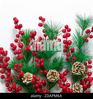 Ornamenti natalizi di acini su sfondo bianco, carta regalo quadrata con decorazioni per le vacanze, coni di pino, rami di abete verde. Tempo invernale sy Foto Stock