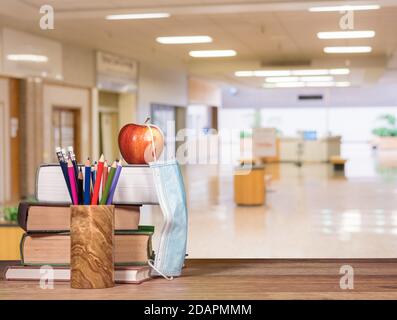 Concetto per il ritorno a scuola con coronavirus o Covid-19 con libri e mela con maschera facciale sullo sfondo della scuola corridoio Foto Stock
