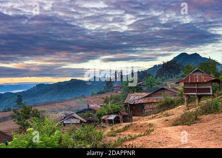 Akha villaggio nelle montagne del Laos del Nord, cielo drammatico del tramonto. Remoto villaggio tribale destinazione di viaggio per trekking tribale, Akha gruppo etnico e. Foto Stock