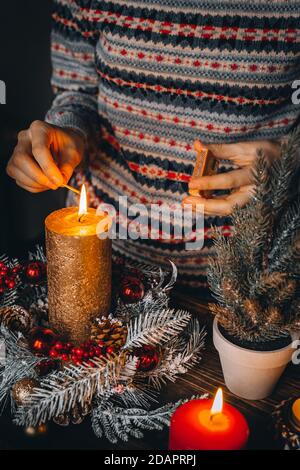 Candele di illuminazione a mano femminile su tavolo decorato a Natale. Candela bruciante di nuovo anno, tempo di avvento, luci calde, decorazioni invernali ornamenti sul vecchio Foto Stock