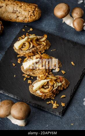 Foto della vita still di deliziosa e sana bruschetta o sandwich con aglio arrosto e funghi champignon sul tavolo blu, testurizzato Foto Stock