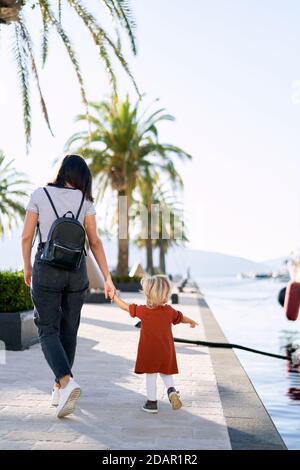 La donna sta camminando mano in mano con il suo bambino vicino le palme su un molo barca Foto Stock