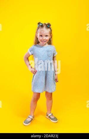 Adorabile bambina in abito alla moda che si pone su sfondo giallo Foto Stock