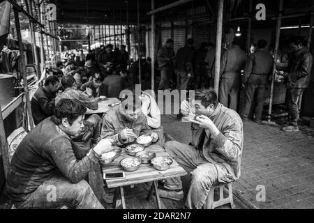 Lavoratore che ha pranzo in uno stallo in un mercato nel centro di Chongqing, dai suoi salari può solo acquistare i pezzi economici di carne, Chongqing, Cina Foto Stock