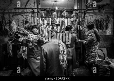 Lavoratore di giorno di fronte a un macellaio in un mercato nel centro di Chongqing, dal suo salario può acquistare solo i pezzi economici di carne, Chongqing Foto Stock