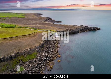 Vista aerea nella luce serale di una cascata che scorre su colonne di basalto nel mare, Norourland eystra, Islanda Foto Stock