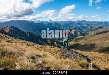 L'escursionista allunga le braccia in aria, sentiero escursionistico fino a ben Lomond, vista sulle montagne, Alpi del Sud, Otago, Isola del Sud, Nuova Zelanda Foto Stock