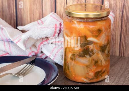 Vasetto di cavolo kimchi, tipico cibo coreano piccante in un ambiente rustico pronto a servire su un piatto. Foto Stock