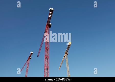 Due gru da costruzione rosse e una gru da costruzione gialla davanti al cielo blu, in Germania Foto Stock