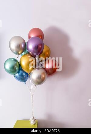 palloncini di elio di colore metallico legati con un arco e tenuti da un peso su un tavolo verde, formato verticale e spazio di copia sulla destra Foto Stock