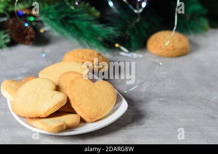 Biscotti fatti in casa a forma di cuore in un piatto bianco sullo sfondo delle decorazioni natalizie. Messa a fuoco selettiva. Foto Stock