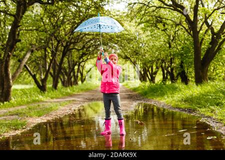 Bambino felice ragazza con un ombrello e stivali di gomma nella pozza su un autunno a piedi Foto Stock