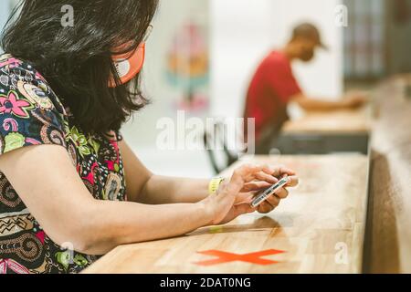 Donna che usa telefoni cellulari per lavorare con immagine sfocata di il contrassegno di posto alternativo per la distanza sociale regola la distanza per uno sedile da altre persone a. Foto Stock