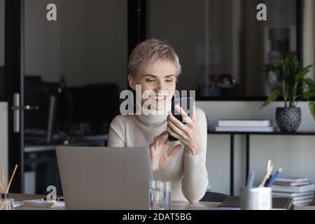 Sorridente giovane donna d'affari con smartphone, seduto alla scrivania Foto Stock